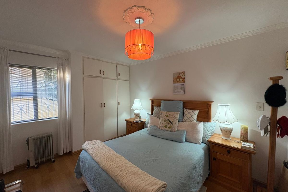 A well-maintained bedroom featuring built-in cupboards, laminate flooring, and decorative ceiling rose detail.
