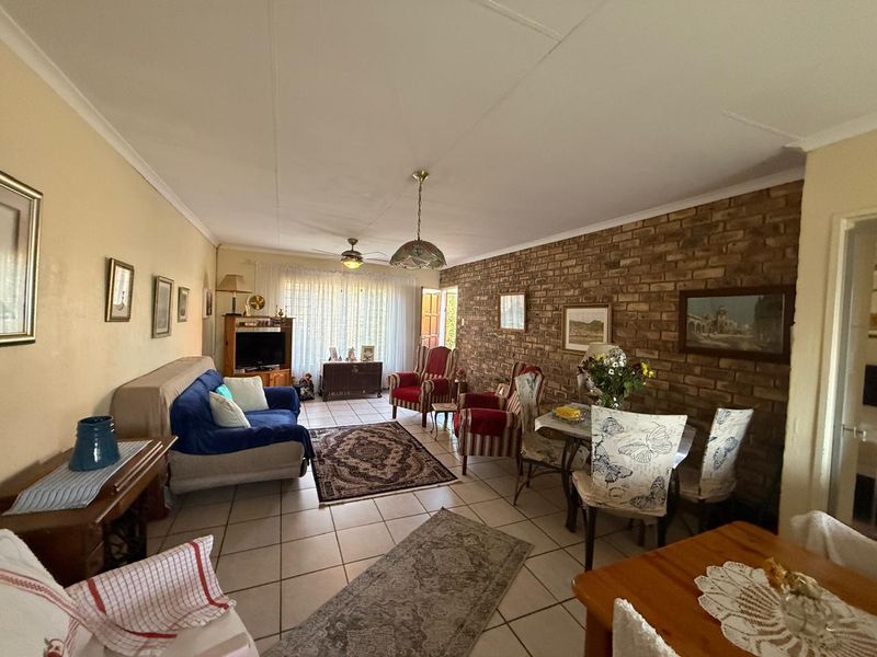 Spacious open-plan living and dining area featuring a rustic exposed brick wall, tiled flooring, and direct access to the outdoor space.