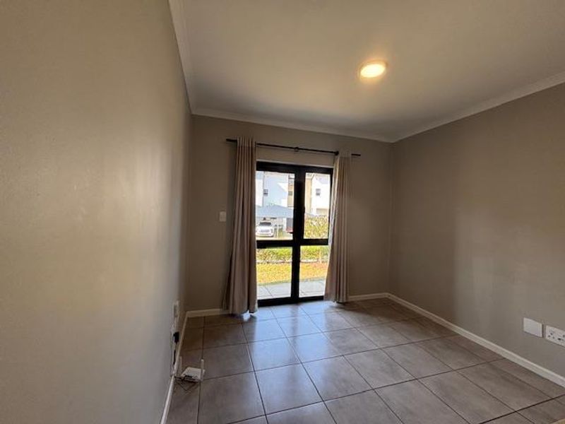 A bright, empty bedroom featuring neutral wall tones, tiled flooring, and a sliding glass door providing access to the exterior.