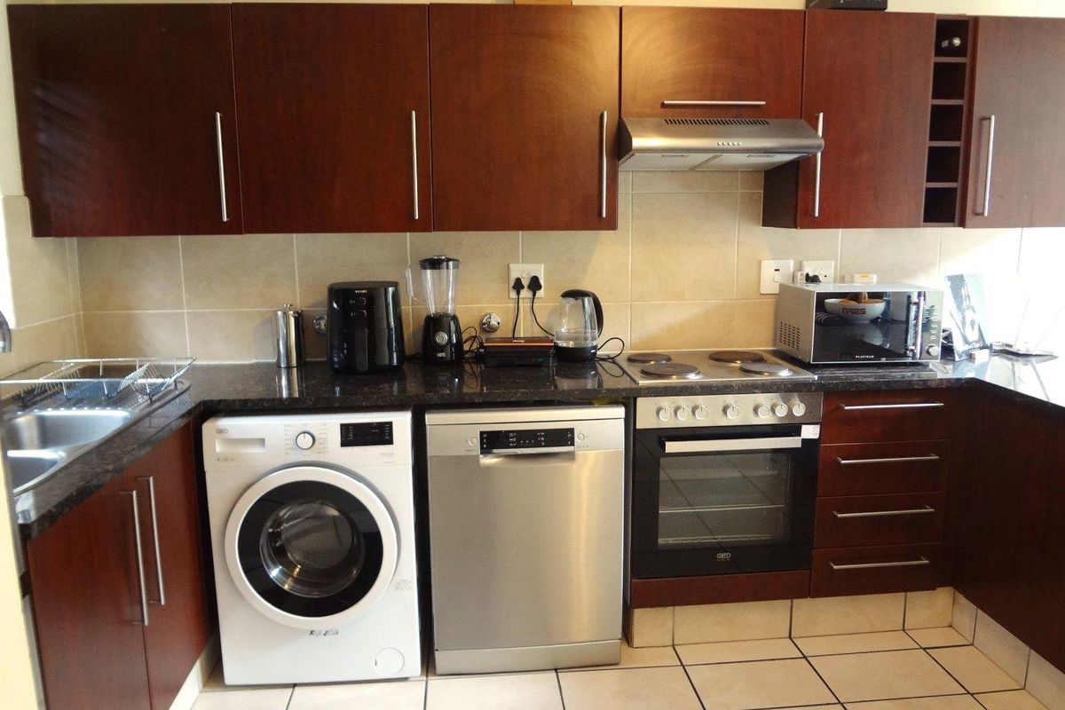 A functional kitchen featuring dark wood cabinetry, granite countertops, tiled backsplash, and integrated stainless steel appliances including an oven and extractor fan.