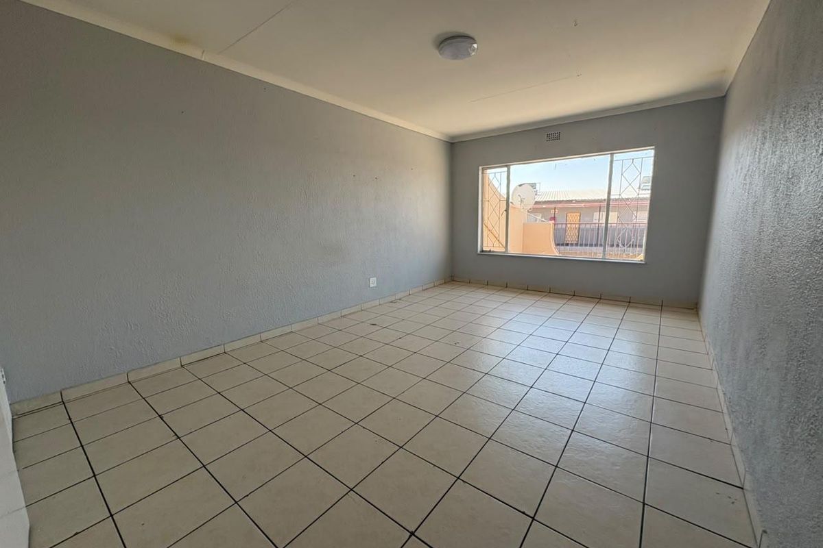 An empty bedroom featuring ceramic floor tiles, security bars on the window, and a neutral wall finish, ready for personalization.