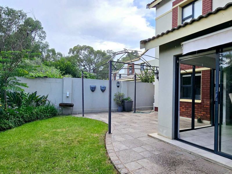A private rear garden featuring a paved patio area, a metal pergola, and direct access to the interior through large sliding glass doors.
