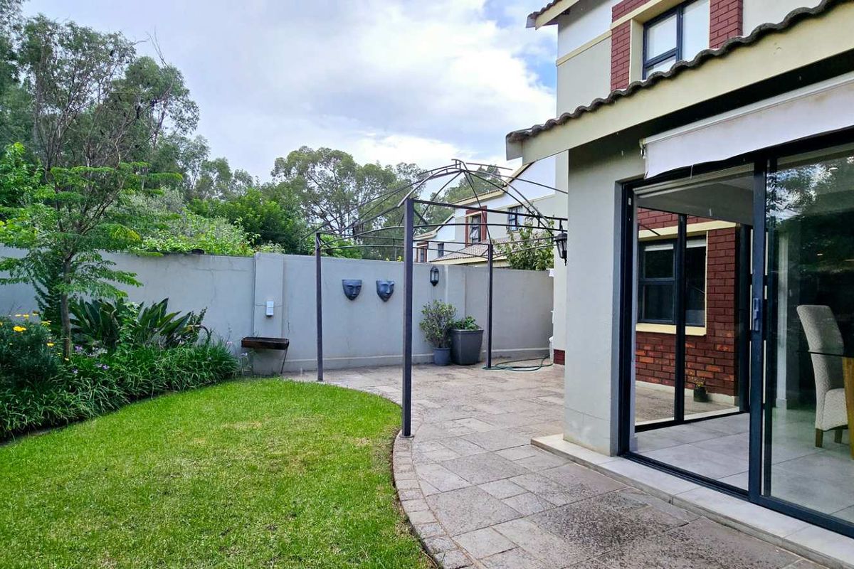 A private rear garden featuring a paved patio area, a metal pergola, and direct access to the interior through large sliding glass doors.