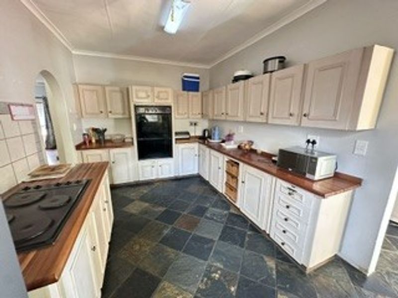 A functional kitchen featuring built-in cabinetry, wooden countertops, an integrated oven, and an electric hob, finished with traditional slate-style floor tiles.