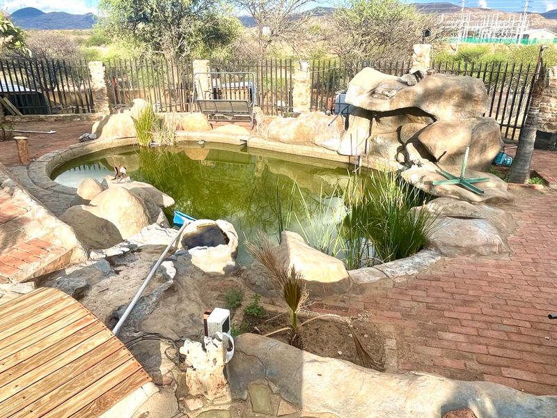 Outdoor rock-feature swimming pool area with brick paving and metal perimeter fencing, requiring maintenance and water treatment.