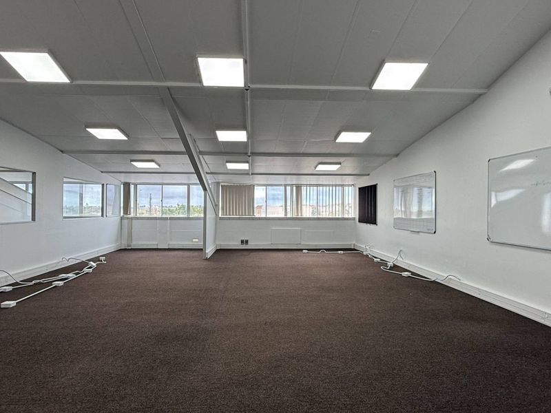 A spacious, open-plan office area featuring recessed LED lighting, wall-mounted whiteboards, and carpeted flooring, providing a functional workspace environment.