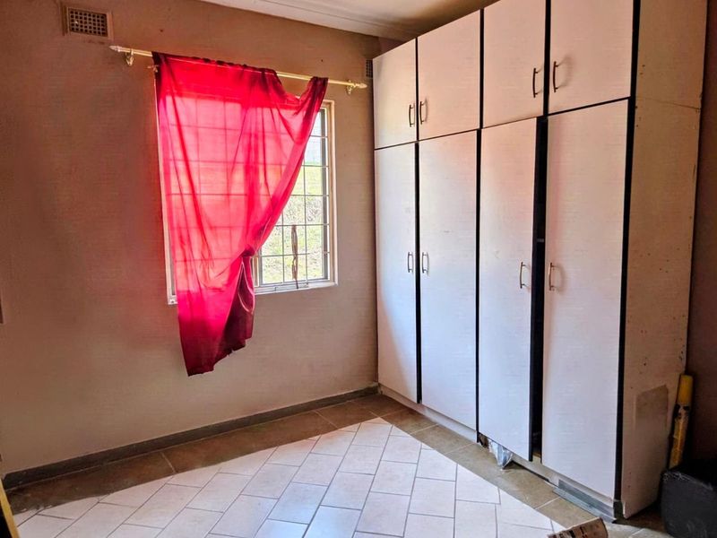 A vacant bedroom featuring built-in cupboards, tiled flooring, and a window with security bars, offering a blank canvas for renovation.