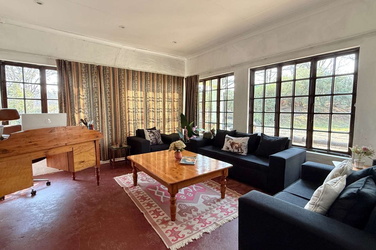Spacious living room featuring large multi-pane windows, recessed lighting, and painted concrete floors, offering a bright space with potential for cosmetic updates.