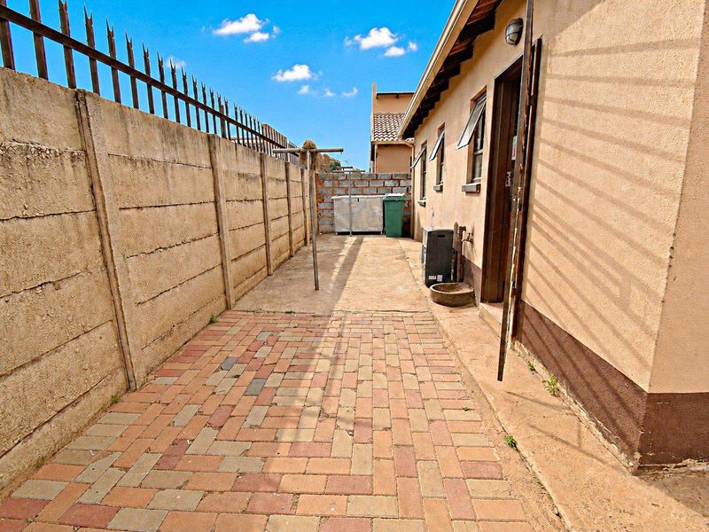 A paved rear exterior side passage featuring a precast concrete boundary wall with security spikes and access to the main dwelling.