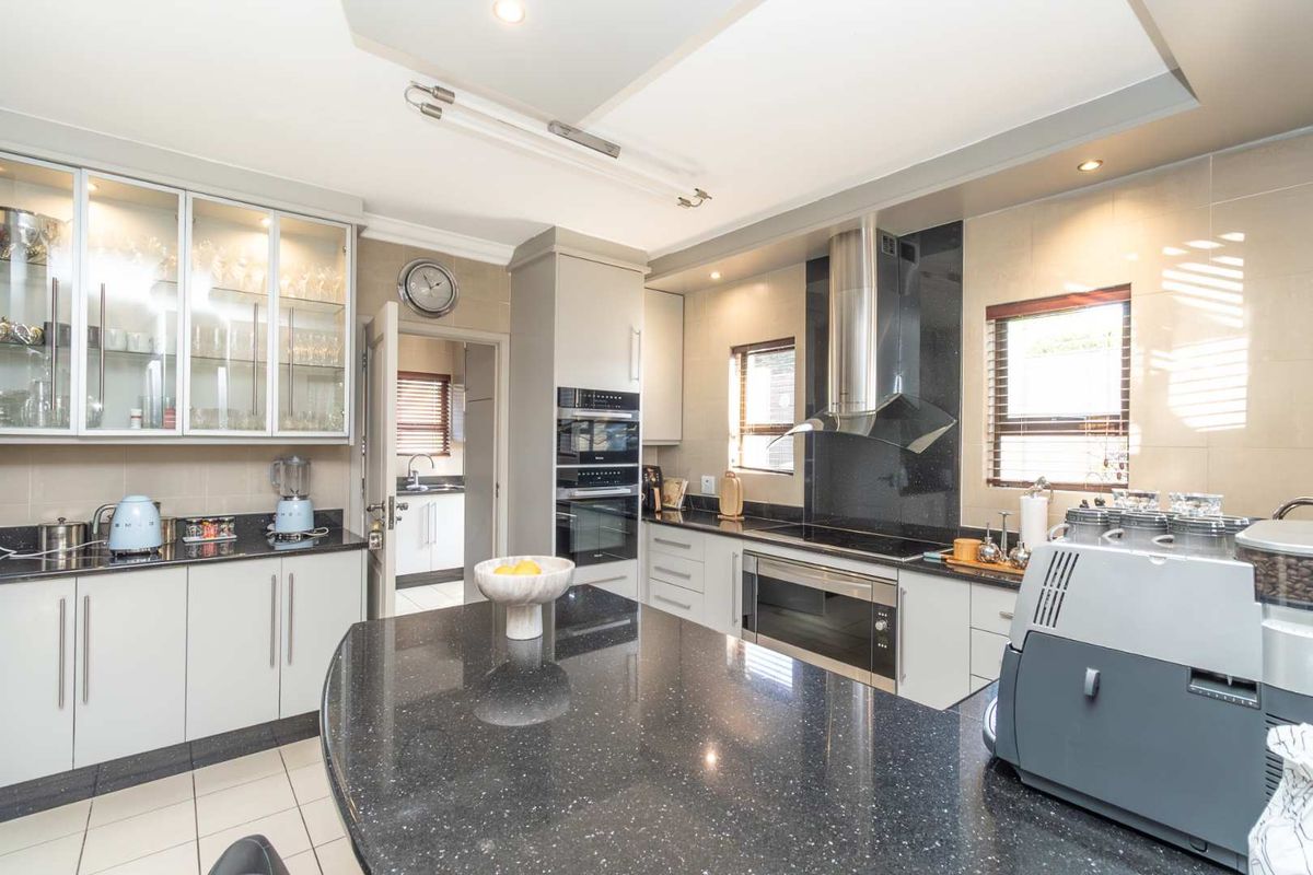 Modern kitchen featuring granite countertops, built-in oven, extractor fan, and glass-fronted cabinetry, with an adjacent scullery area visible.