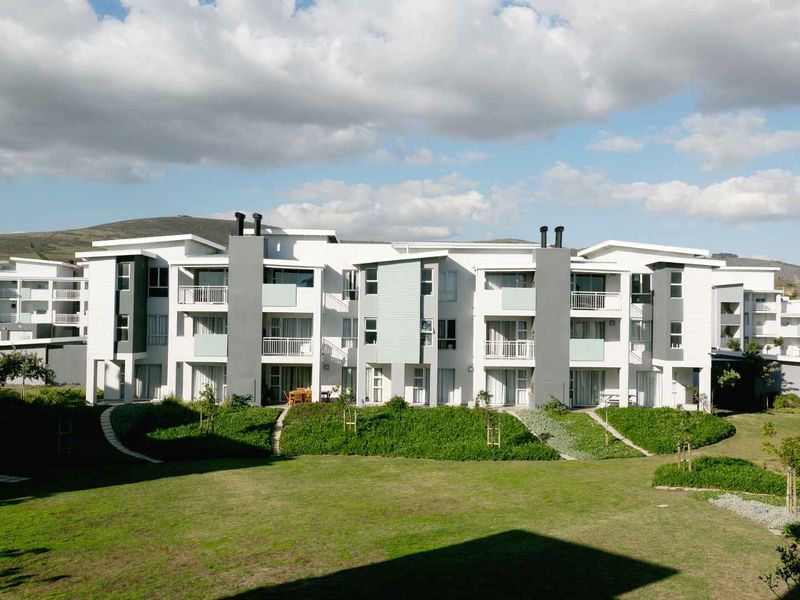 A view of the rear elevation of a modern apartment complex featuring balconies, sliding glass doors, and well-maintained communal garden areas.