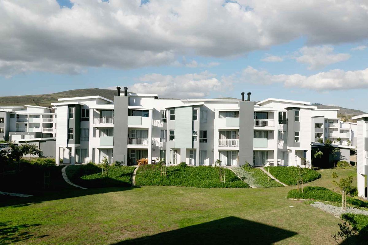 A view of the rear elevation of a modern apartment complex featuring balconies, sliding glass doors, and well-maintained communal garden areas.