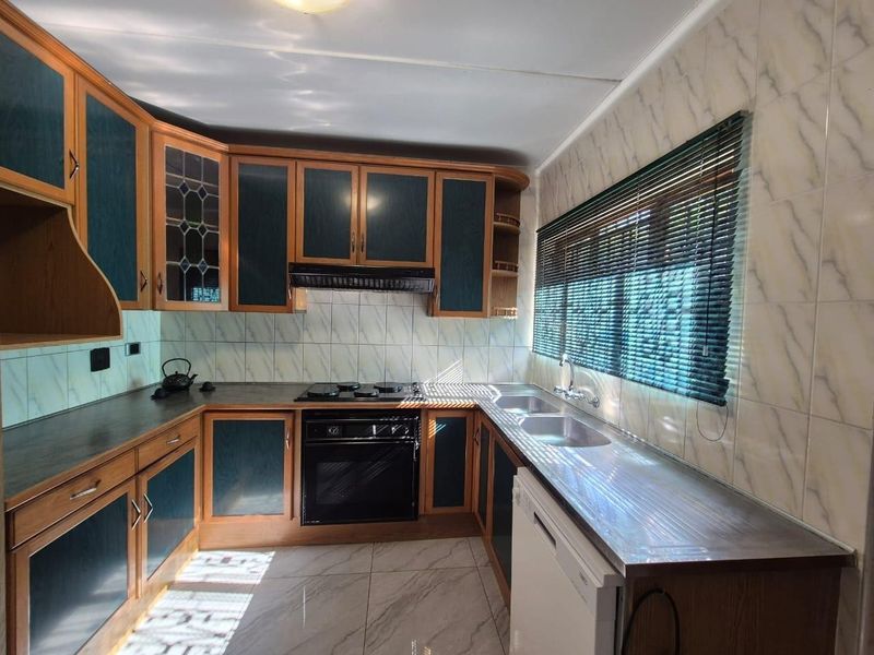 A functional kitchen featuring wood-toned cabinetry with dark inserts, tiled splashbacks, a built-in oven and hob, and a double bowl sink.