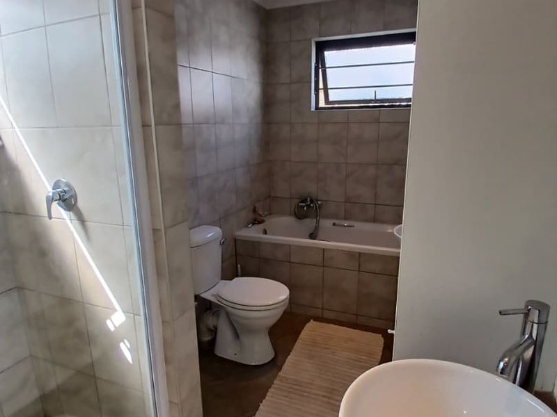 A functional bathroom featuring a glass shower enclosure, a bathtub, and a modern vessel sink with tiled finishes throughout.