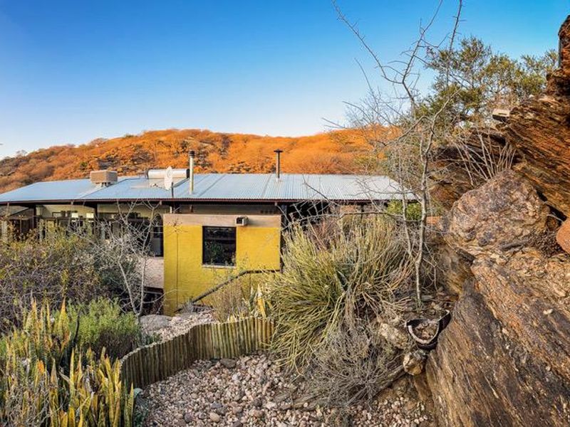 A rear view of a house featuring a corrugated metal roof, solar water heater, and natural rock landscape setting.