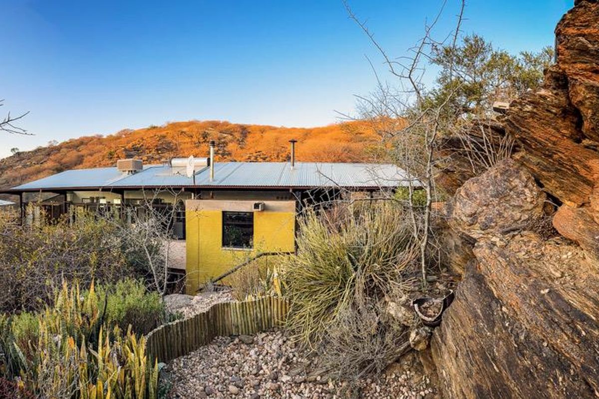 A rear view of a house featuring a corrugated metal roof, solar water heater, and natural rock landscape setting.