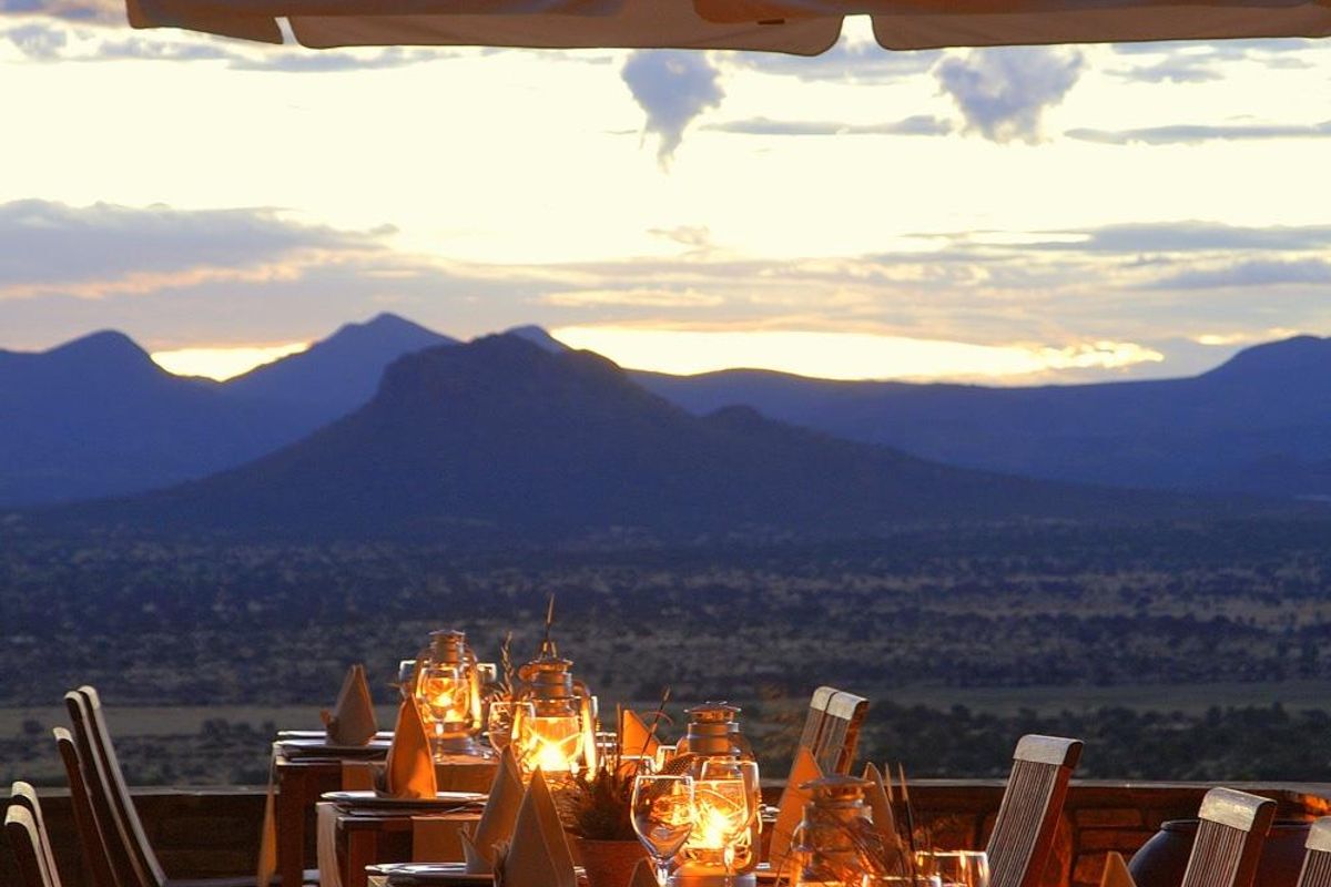 An outdoor dining terrace featuring a covered patio area with expansive, panoramic views of the surrounding mountain landscape and nature reserve.