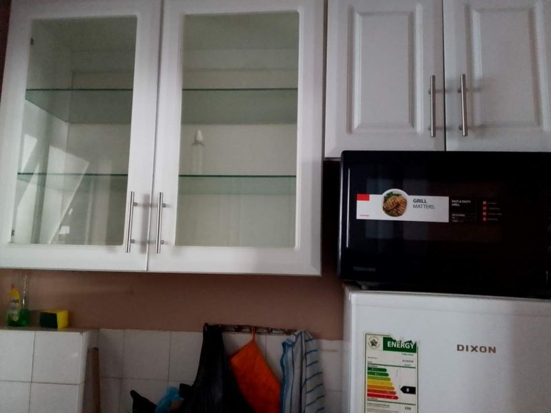 A kitchen area featuring white shaker-style cabinetry with glass-fronted upper units and a tiled backsplash, showing signs of wear.
