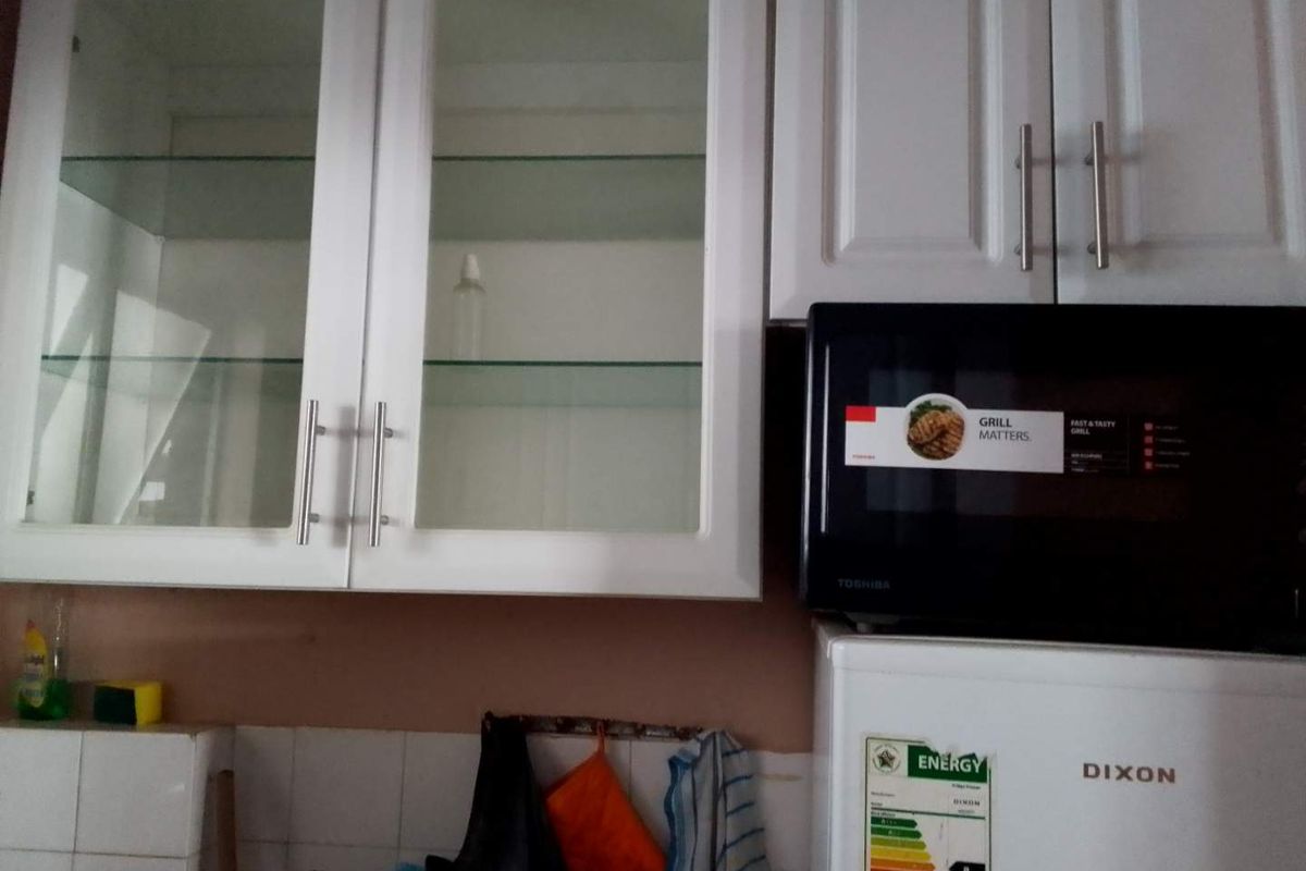 A kitchen area featuring white shaker-style cabinetry with glass-fronted upper units and a tiled backsplash, showing signs of wear.
