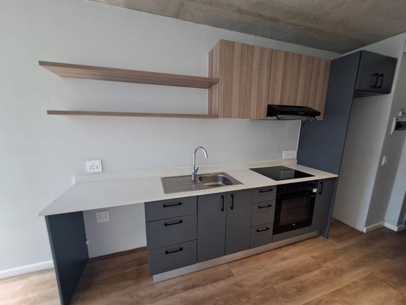 Modern kitchen featuring sleek grey and wood-tone cabinetry, integrated electric oven and hob, stainless steel sink, and minimalist floating shelves.