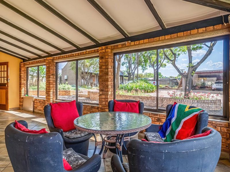 A covered patio area featuring exposed brick walls, tiled flooring, and large glass windows overlooking the garden.