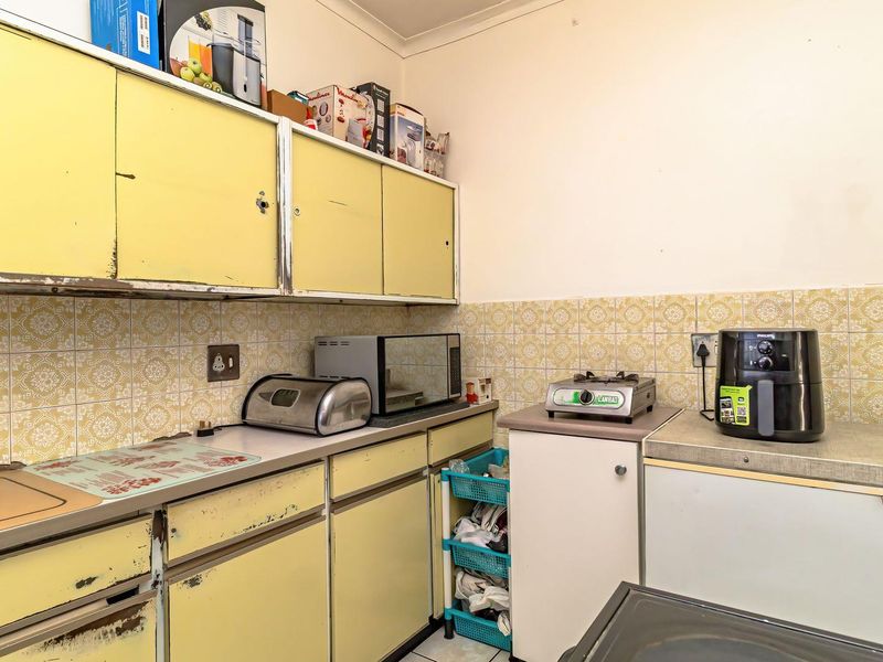 A dated kitchen featuring original yellow cabinetry, tiled backsplash, and laminate countertops, offering significant potential for a modern renovation.