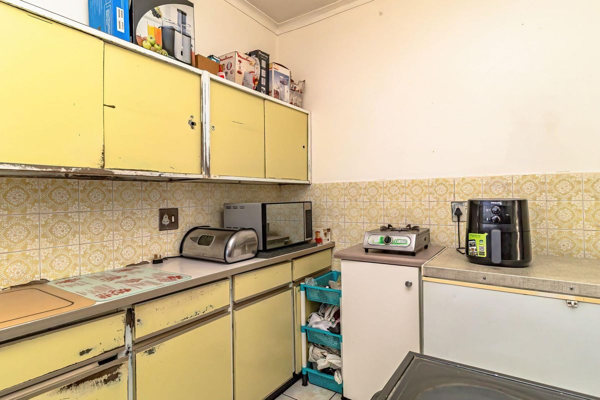 A dated kitchen featuring original yellow cabinetry, tiled backsplash, and laminate countertops, offering significant potential for a modern renovation.