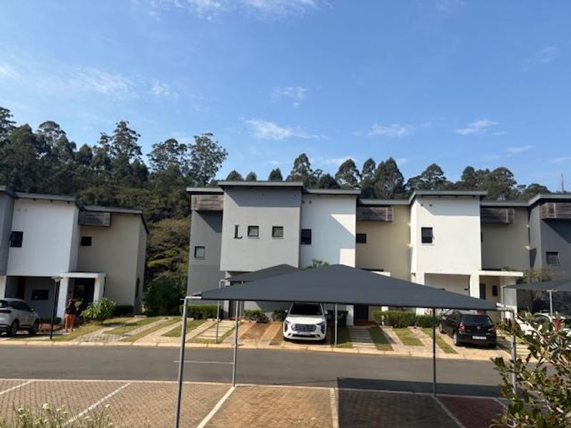 Front elevation of a modern apartment complex featuring paved driveways and dedicated shade cloth carports under a clear blue sky.