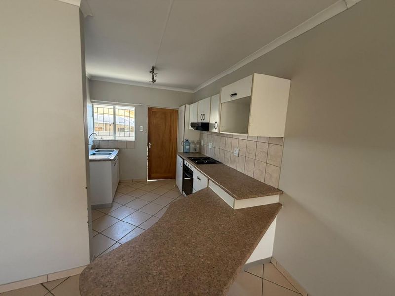 A functional kitchen featuring built-in cabinetry, laminate countertops, a hob, oven, extractor fan, and a double sink with tiled flooring and backsplash.
