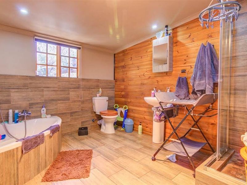 Spacious bathroom featuring timber wall paneling, a bathtub, a separate shower enclosure, and a pedestal sink with tiled flooring.