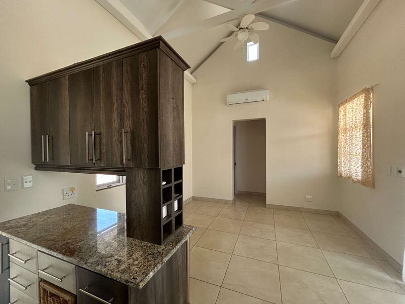 Open-plan living area featuring a modern kitchen with granite countertops, vaulted ceilings, tiled flooring, and a split-system air conditioner.