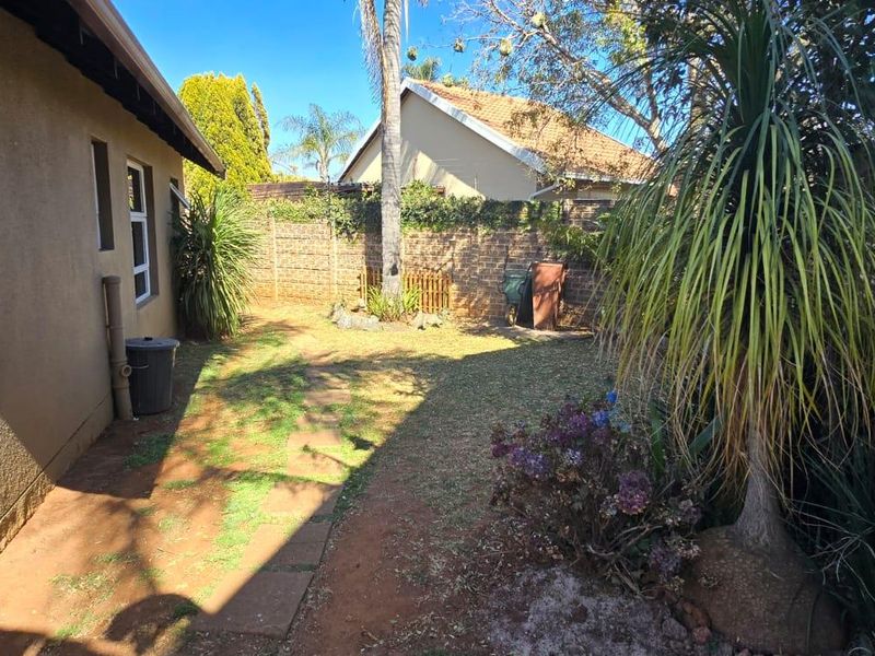 A private rear garden area featuring a paved walkway, established trees, and brick boundary walls, offering potential for landscaping improvements.