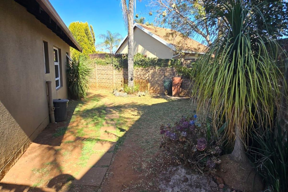 A private rear garden area featuring a paved walkway, established trees, and brick boundary walls, offering potential for landscaping improvements.