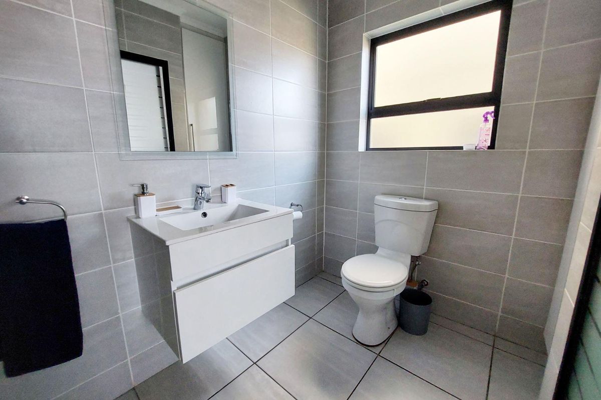 Modern bathroom featuring a wall-mounted vanity with basin, chrome fixtures, neutral grey wall and floor tiles, and a window for natural light.