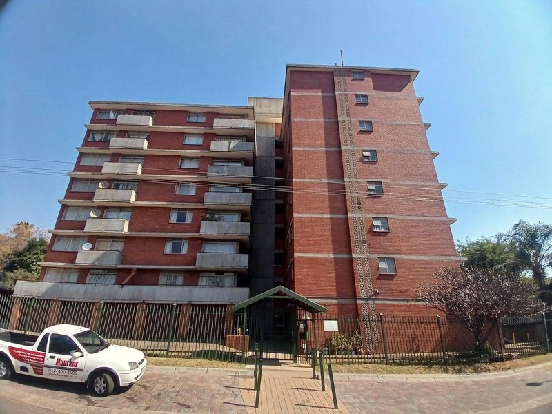 Front elevation of a multi-story brick apartment building featuring private balconies, secure perimeter fencing, and a gated pedestrian entrance.
