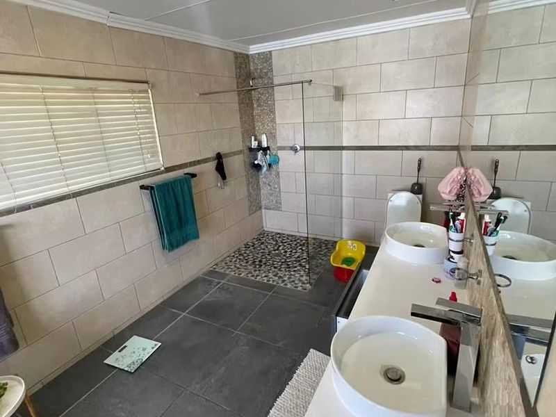 Modern bathroom featuring a double vanity with vessel sinks, a spacious walk-in shower with pebble flooring, and a wall-mounted toilet.