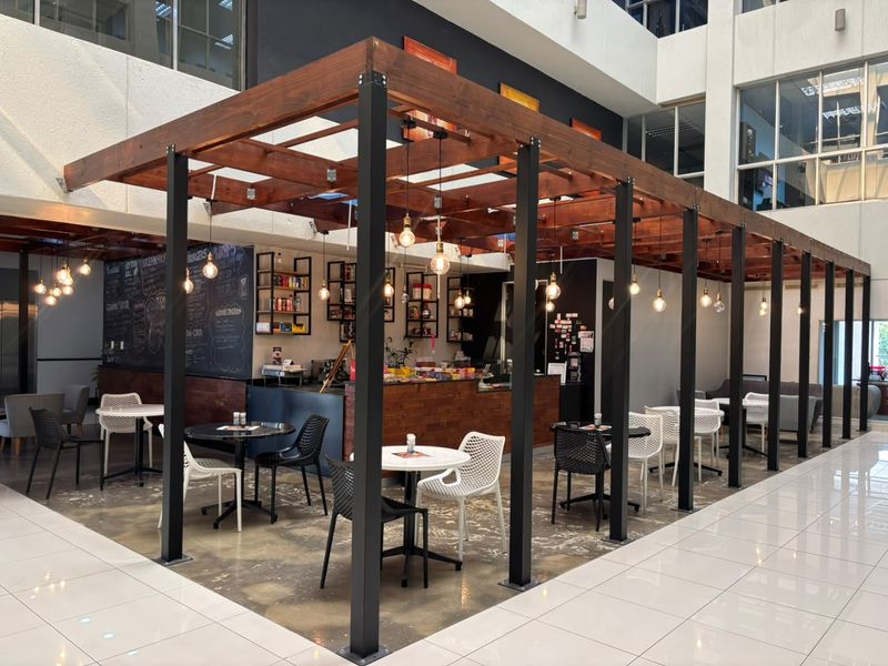 Modern open-plan office cafe area featuring a timber pergola structure, polished concrete floors, and integrated service counter with pendant lighting.