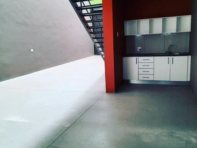 A compact kitchenette area featuring white built-in cabinetry, a sink, and a modern metal staircase within an industrial-style open space.