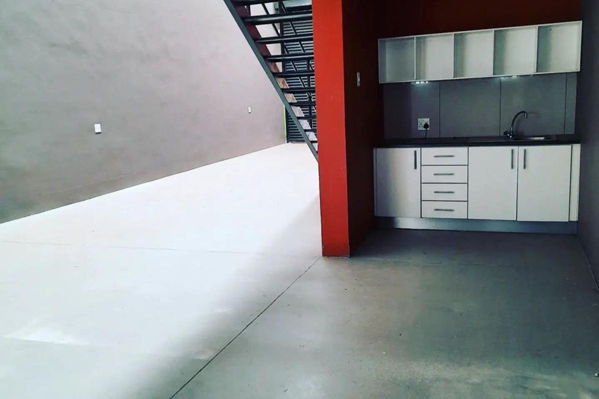 A compact kitchenette area featuring white built-in cabinetry, a sink, and a modern metal staircase within an industrial-style open space.
