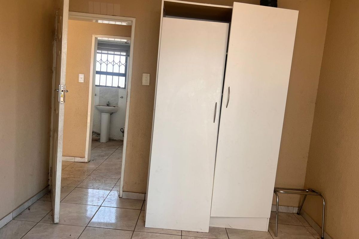 A bedroom featuring tiled flooring and a built-in wardrobe, with an adjacent bathroom visible through the doorway.