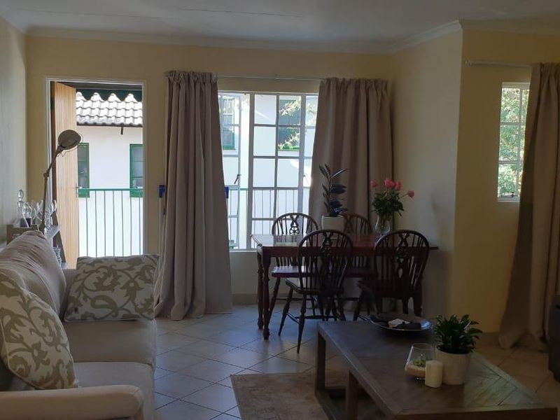 A comfortable living and dining area featuring tiled flooring, natural light from large windows, and direct access to an outdoor balcony space.