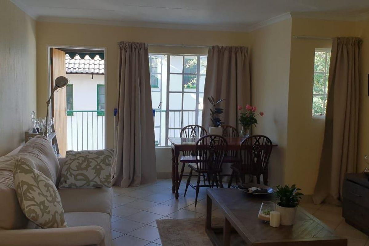 A comfortable living and dining area featuring tiled flooring, natural light from large windows, and direct access to an outdoor balcony space.