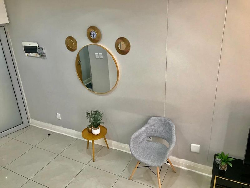 A clean, neutral-toned hallway featuring large format floor tiles, skirting boards, and a wall-mounted electrical distribution board.
