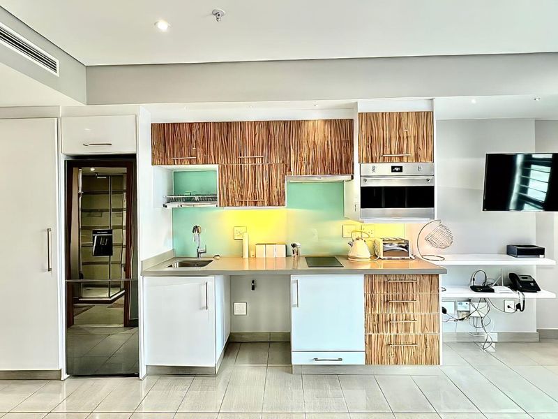 Modern kitchen featuring wood-grain and white cabinetry, integrated oven, glass splashback, and stainless steel sink, set within a clean, contemporary open-plan living space.