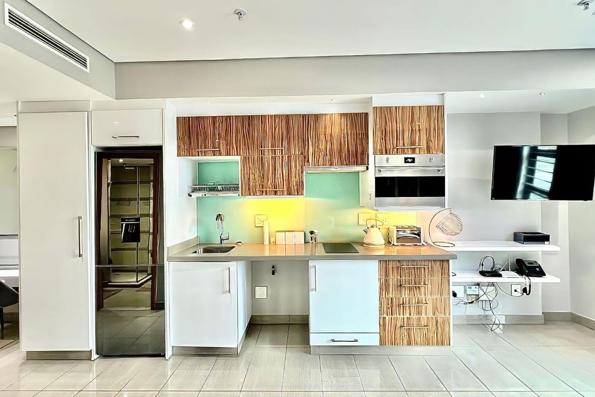 Modern kitchen featuring wood-grain and white cabinetry, integrated oven, glass splashback, and stainless steel sink, set within a clean, contemporary open-plan living space.