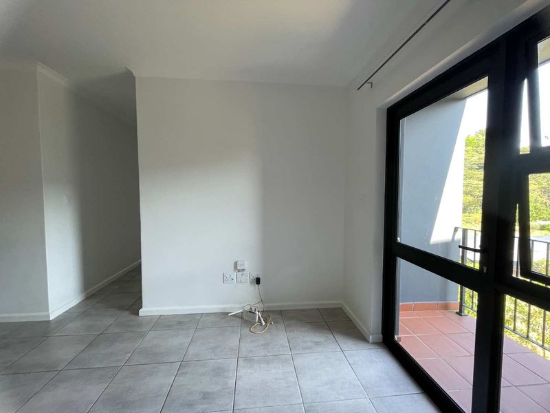 An empty living area featuring neutral tiled flooring and a large sliding door providing access to a private balcony.