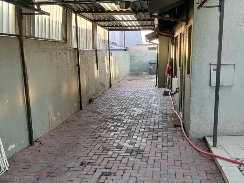 A covered outdoor parking area featuring a metal carport structure and paved flooring, showing signs of wear and requiring maintenance.