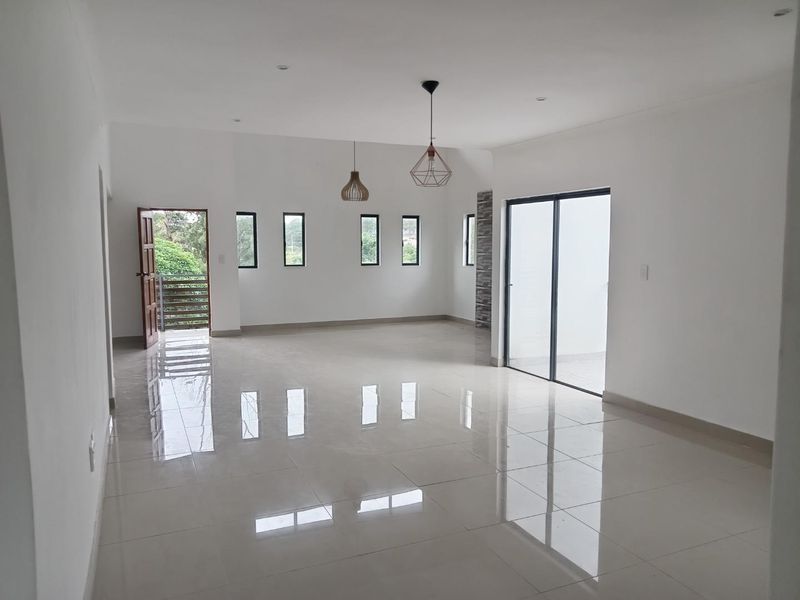 A bright, spacious, and empty open-plan living area featuring polished tiled floors, modern pendant lighting, and a sliding glass door leading to an outdoor space.
