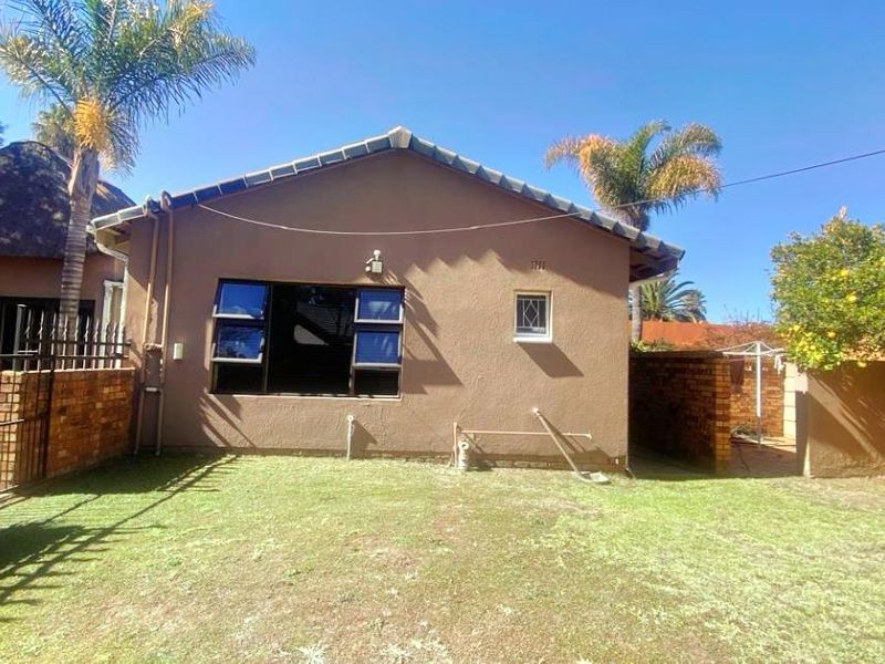 Rear view of the house featuring a plastered exterior, tiled roof, and a private garden area with brick boundary walls.