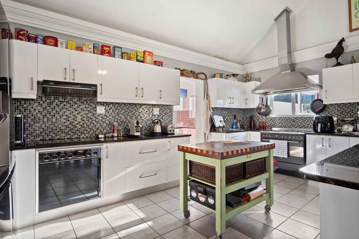 A well-equipped kitchen featuring white cabinetry, granite countertops, a mosaic tile backsplash, and a stainless steel extractor fan with a vaulted ceiling.